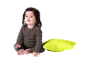 Baby im braunen Strampler sitzt neben einem leuchtend grünen Kissen.
