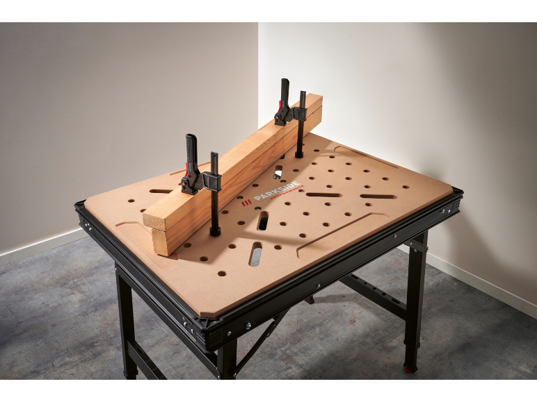 Werkbank mit perforierter Platte und zwei Klemmen, die einen Holzbalken halten.