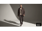 Ein Mann in einer braunen Daunenjacke, einem beigen Pullover und einer braunen Hose geht in einem Studio.