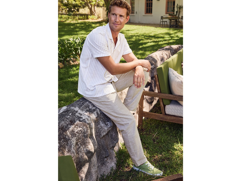 Mann in einem gestreiften Hemd, beigen Hosen und grünen Sneakern im Garten.