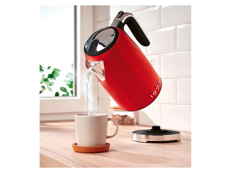Roter Wasserkocher mit „1973“-Aufschrift gießt Wasser in eine Tasse auf einer Holztheke.