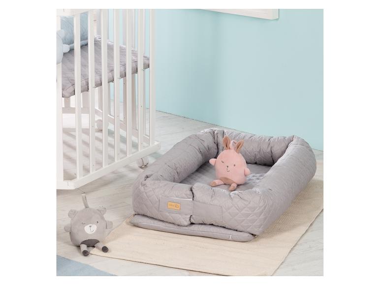 Babynest mit rosa Häschen und grauem Teddybär Plüschtieren neben einem weißen Babybett