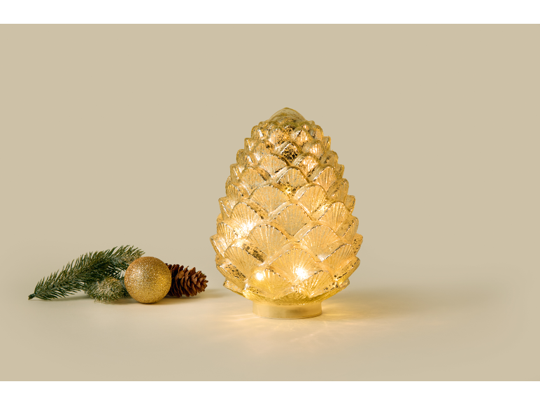 Leuchtender dekorativer Glas-Tannenzapfen mit Weihnachtsdekoration daneben.
