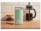 Mintgrüne Kaffeemühle, French Press Kaffeemaschine und Kaffeepulverglas auf einem Holztisch.