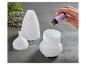 Eine Hand tropft Lavendelöl in einen weißen Aroma-Diffusor, mit getrocknetem Lavendel im Hintergrund.