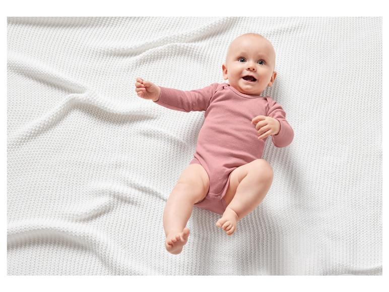 Ein Baby in einem rosafarbenen Strampler auf einer weißen Decke