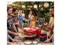 Gruppe Freunde bei einer DIY-Pizzaparty im Garten, mit Pizzaofen und Getränken.