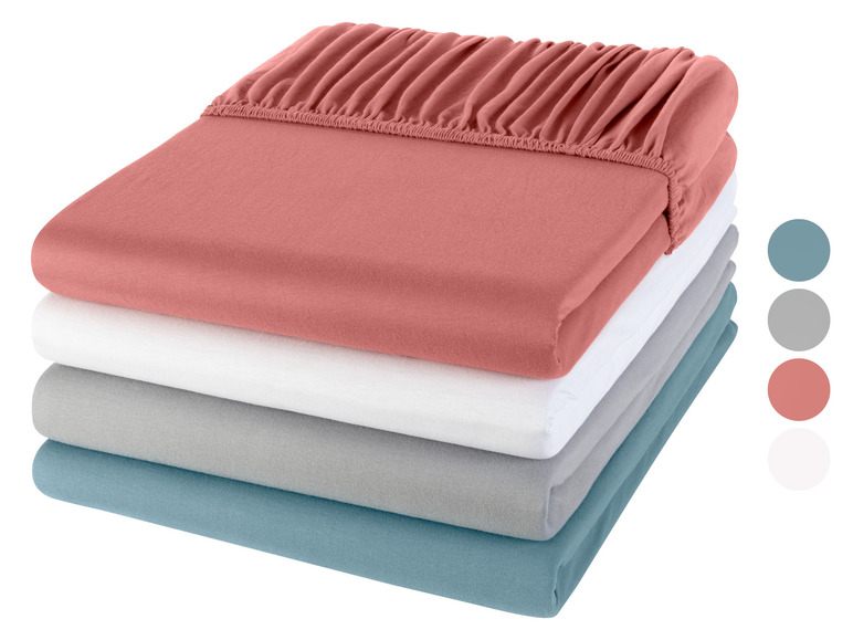 Ein Stapel Bettwäsche in verschiedenen Farben: rosa, weiß, grau und blau.