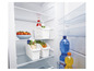 Weiße Aufbewahrungskörbe in einem Kühlschrank mit Wasserflaschen, Saft und Gemüse.