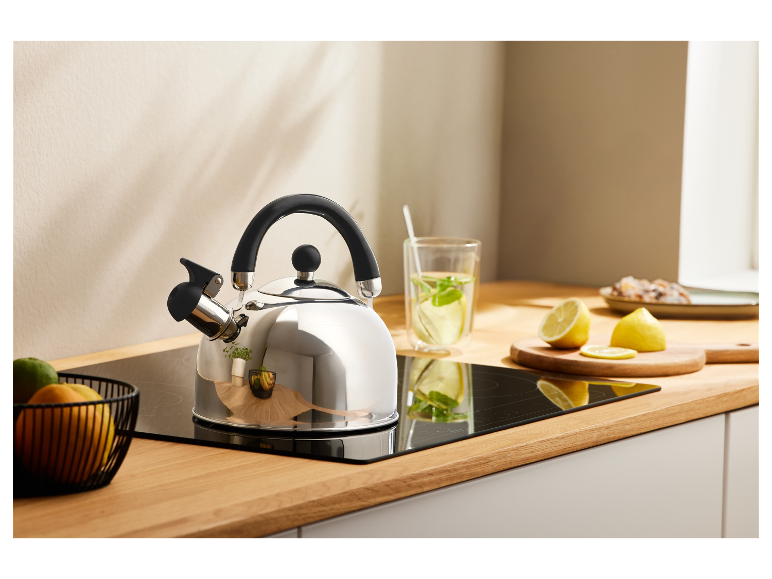Edelstahl-Wasserkocher mit schwarzem Griff auf einem Induktionskochfeld in einer Küche.