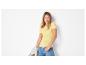 Frau in gelbem Ripp-T-Shirt und blauen Jeans, hält eine beige Jacke.