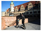 Ein Mann mit Helm und Lederjacke hält ein 'SacherRad' Elektrofahrrad in der Stadt.