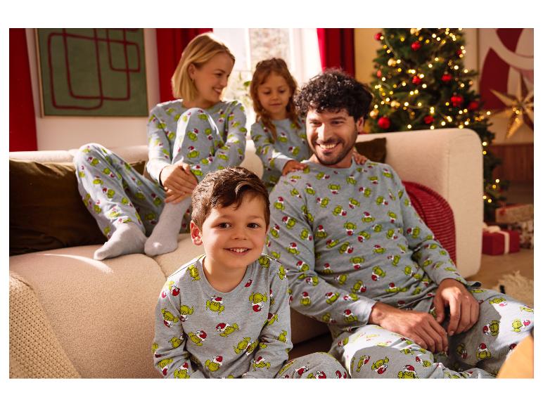 Familie in passenden Grinch-Pyjamas sitzt auf einem Sofa neben einem Weihnachtsbaum.
