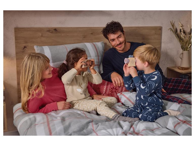 Eine Familie im Schlafanzug auf einem Bett, Kinder spielen mit Spielzeugkameras.