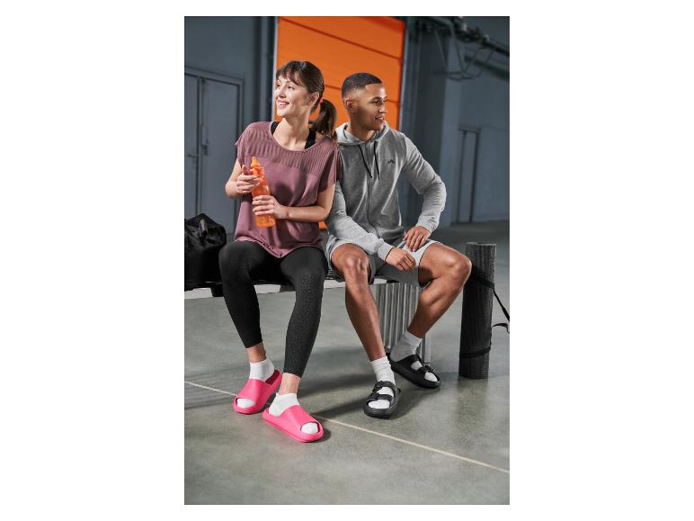 Frau und Mann in Sportkleidung und Badeschlappen sitzen nach dem Training auf einer Bank.