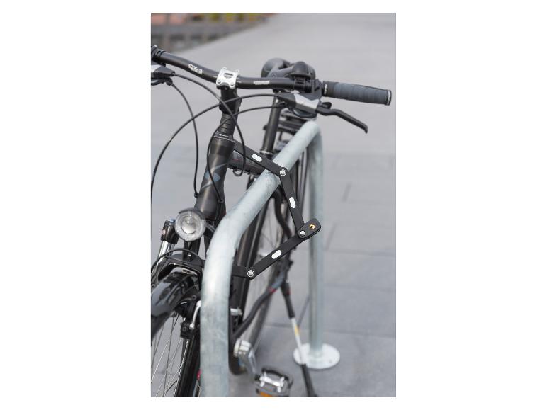Ein schwarzes Fahrrad mit einem Faltschloss, das an einem Metallfahrradständer befestigt ist.