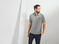 Ein Mann trägt ein graues Poloshirt mit einem kleinen dreieckigen Logo.