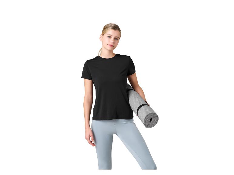 Frau in schwarzem T-Shirt und hellblauen Leggings hält eine Yogamatte.