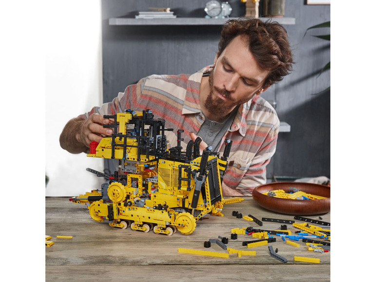 Ein Mann baut einen gelben LEGO Technic Bulldozer.