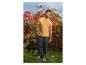 Mann in gelbem T-Shirt und dunkelgrüner Hose vor Blumen.