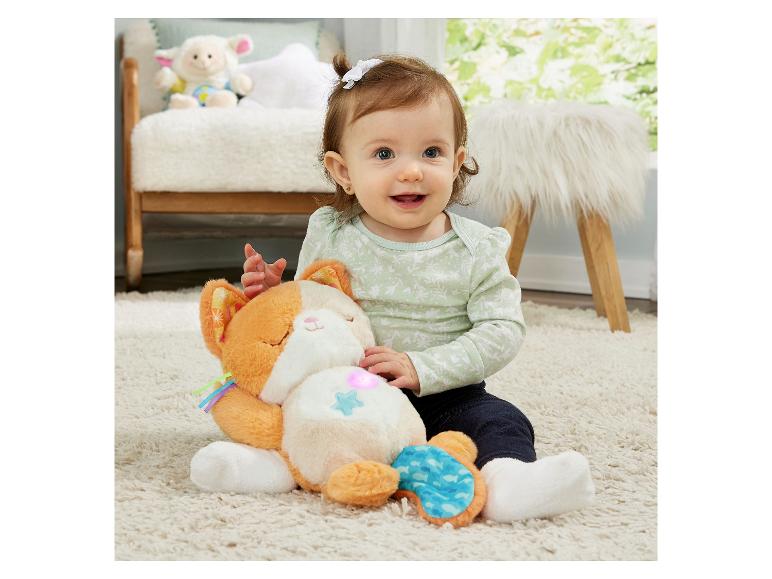 Lächelndes Baby sitzt auf Teppich mit Plüschkatze mit leuchtendem Bauch.