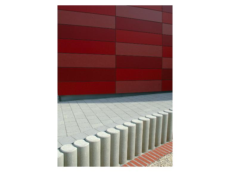 Rote Fassade mit horizontalen Paneelen, graue Pflastersteine und eine Reihe Betonpoller.