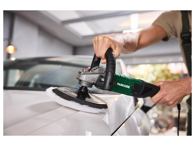 Mann poliert ein weißes Auto mit einer Poliermaschine in einer Garage.