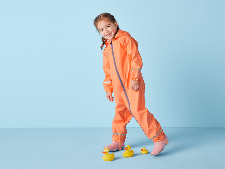 Ein Kind in einem orangen Regenanzug und rosafarbenen Gummistiefeln geht mit Gummienenten spazieren.