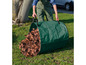 Eine Person entleert einen grünen Gartensack voller Blätter.