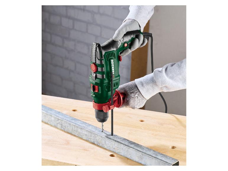 Schlagbohrmaschine in Händen, bohrt in ein Metallprofil auf einem Holztisch.