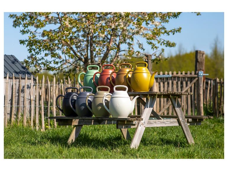 Bunte Garten-Gießkannen auf einem Holztisch unter einem blühenden Baum.