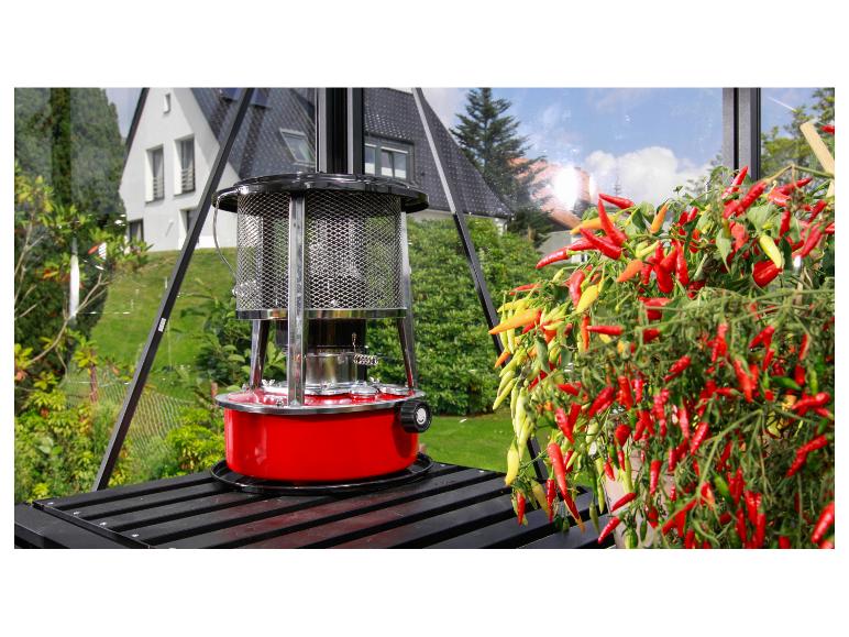 Roter Gewächshausheizer neben einer lebhaften Chilipflanze im Gewächshaus.