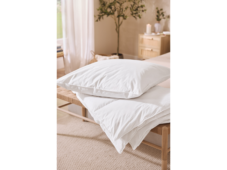 Weiße Kissen und Bettdecken auf einer Bank in einem hellen Schlafzimmer.