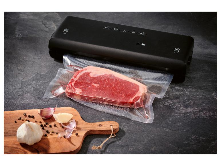 Schwarzes Vakuumiergerät mit einem vakuumverpackten Stück Rindfleisch und Knoblauch auf einem Schneidebrett.