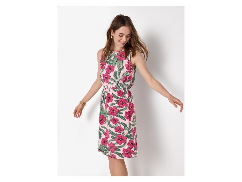 Frau in einem rosa Blumen-Sommerkleid mit grünen Blättern, lächelnd und nach unten schauend.