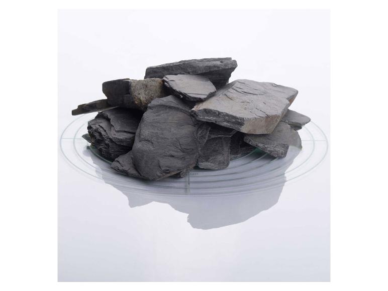 Ein Haufen dunkler, flacher Schiefersteine auf einer transparenten, runden Platte.