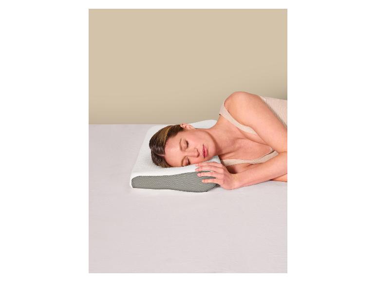 Frau schläft auf der Seite auf einem ergonomischen Kissen in einem Bett mit weißen Laken.