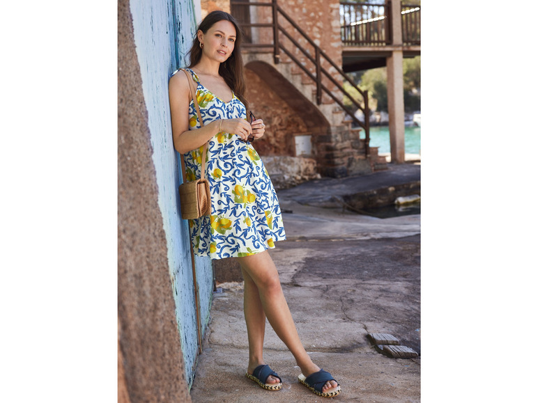 Eine Frau in einem weißen Kleid mit Blumenmuster und Espadrilles.