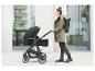 Frau in Mantel und mit Rucksack spaziert mit Kinderwagen.