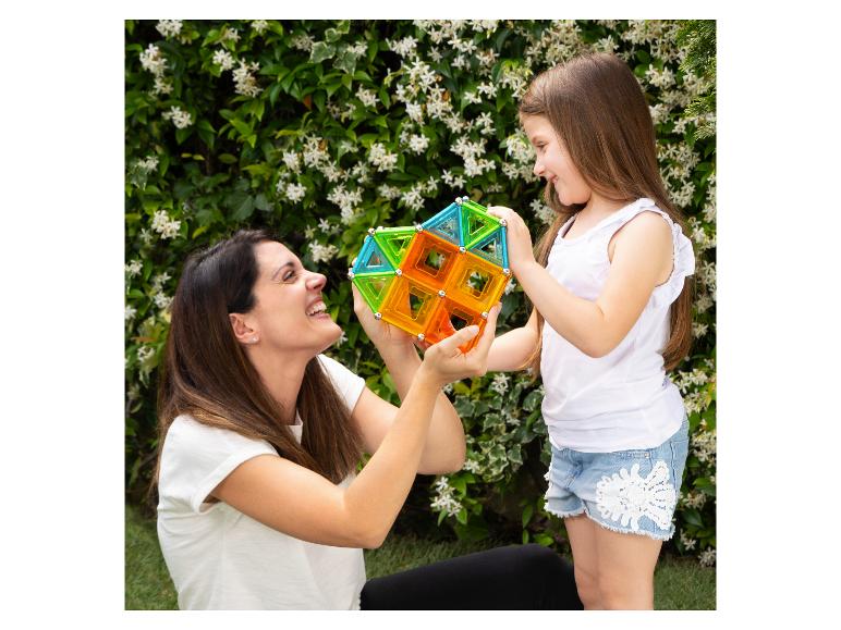 Lächelnde Mutter und Tochter spielen mit bunten Magnetbausteinen im Garten.