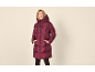 Frau in langer bordeauxroter Steppjacke, Hände in den Taschen, lächelnd.