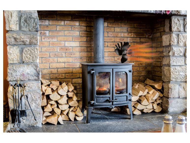 Holzofen mit Ventilator, Brennholz und Kaminbesteck.