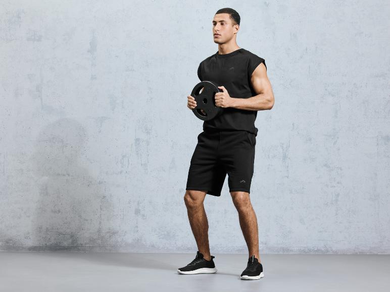 Ein Mann in schwarzen Sport-Shorts und einem Shirt, der eine Gewichtsscheibe hält.