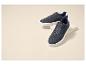 Zwei blaue Wildleder-Sneaker mit weißen Sohlen, auf einem beigen Podest platziert.