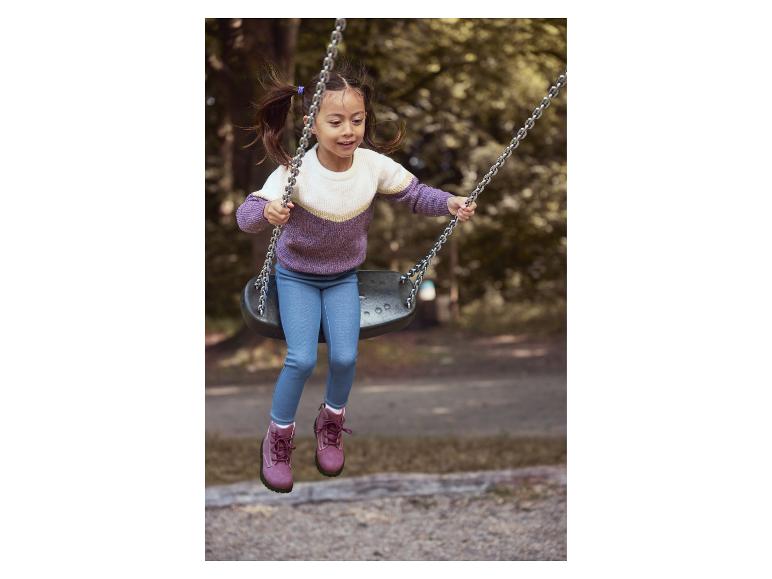 Glückliches Mädchen in lila-weißem Pullover und blauen Jeans schaukelt in einem Park.