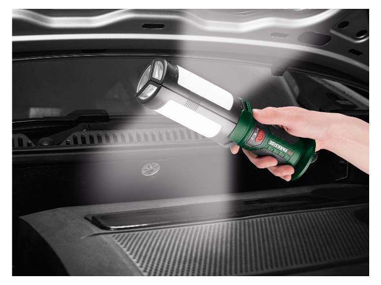 Eine Hand hält eine Parkside Arbeitsleuchte, die in ein Auto leuchtet.