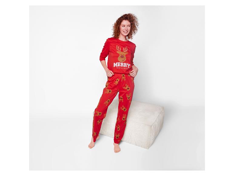 Frau mit roten Locken in einem roten Weihnachtspyjama mit Rentieren, steht neben einem Hocker.