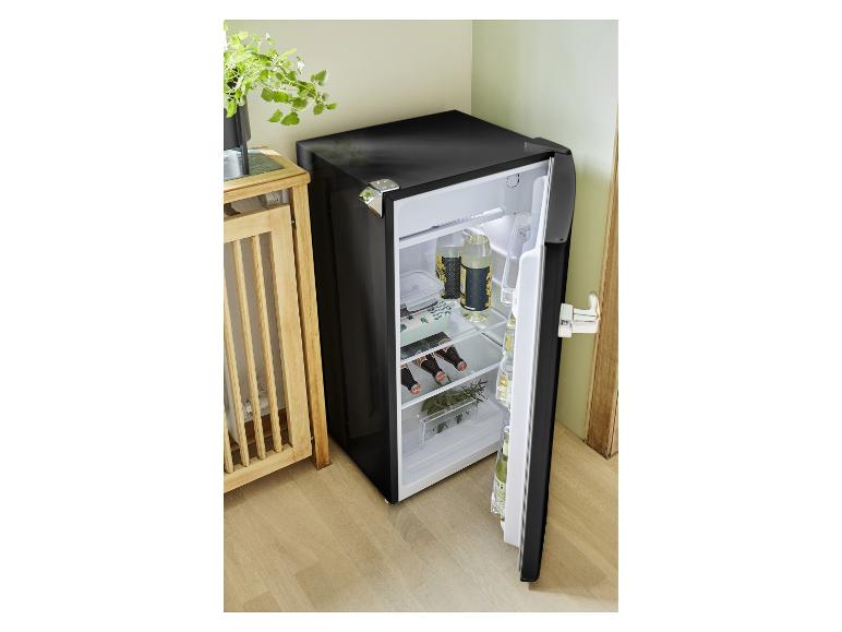 Offener schwarzer Minikühlschrank mit Getränken und Essen, neben einem Holztisch.