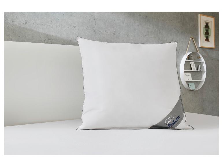 Weißes Kissen mit grauem Rand und „135 Jahre Balette“-Logo auf einem weißen Bett.