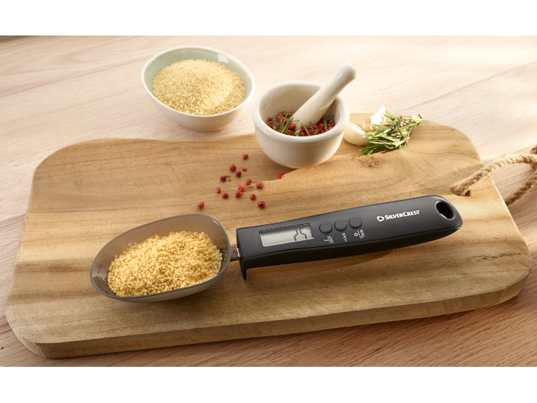 Digitale Messlöffelwaage mit Couscous auf einem Holzbrett mit Gewürzen